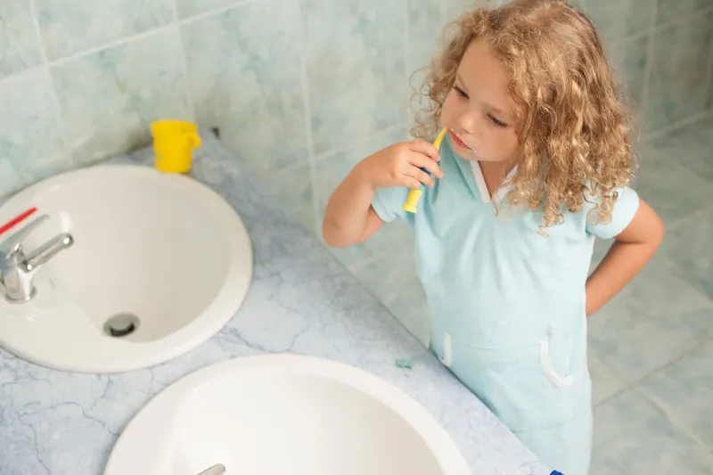 Child brushing teeth by sink, highlighting personal hygiene habits