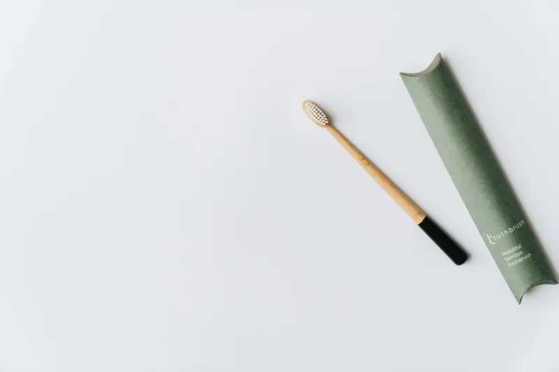 Minimalist bamboo toothbrush with green eco-friendly packaging on white background