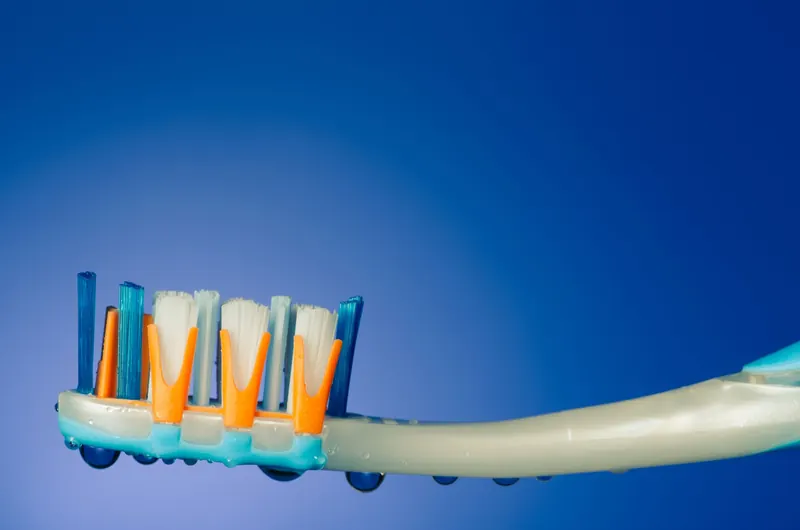 Detailed view of a toothbrush with multicolored bristles and water droplets on a blue background