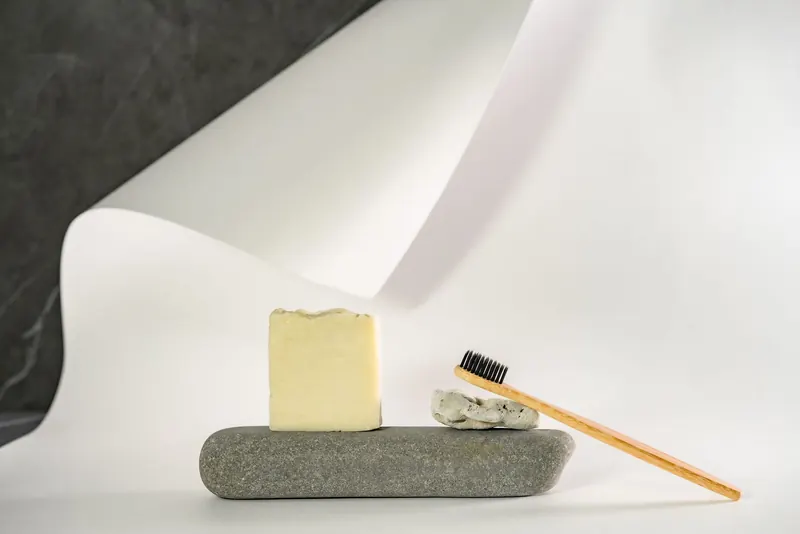 A minimalist arrangement of a soap bar and bamboo toothbrush on a white surface