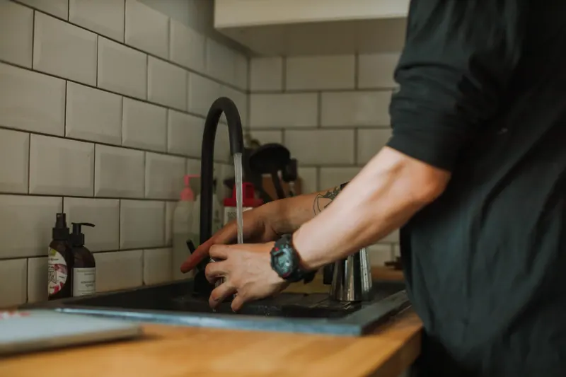 Close-up of a person washing hands at a sink with running water, wearing a wristwatch