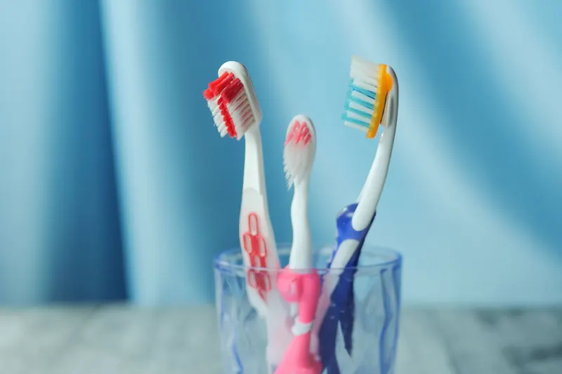 A trio of vibrant toothbrushes in a glass on a blue background, emphasizing dental hygiene