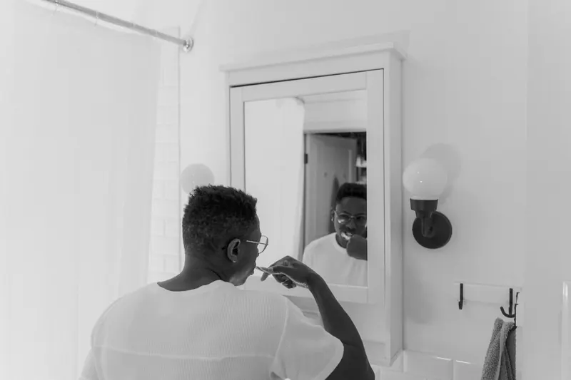 A black and white photo of a man brushing his teeth in front of a bathroom mirror