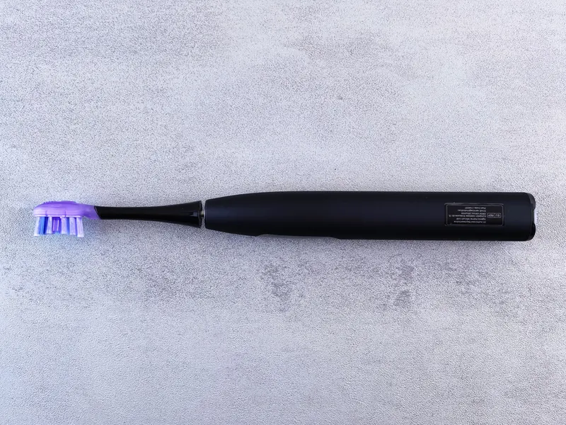 A sleek black electric toothbrush with a purple head lies on a textured concrete surface