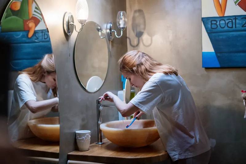 A woman brushing her teeth in a cozy, modern bathroom with warm lighting and artistic decor